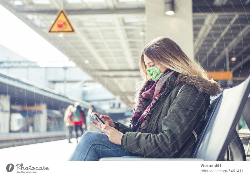 Junge Frau mit Smartphone mit Maske am Bahnsteig Leute Menschen People Person Personen Europäisch Kaukasier kaukasisch 1 Ein ein Mensch eine nur eine Person