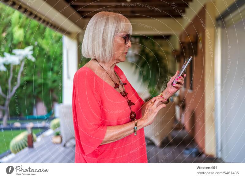 Stylische ältere Frau, die ein Smartphone benutzt, während sie auf der Terrasse steht Farbaufnahme Farbe Farbfoto Farbphoto Spanien Freizeitbeschäftigung Muße