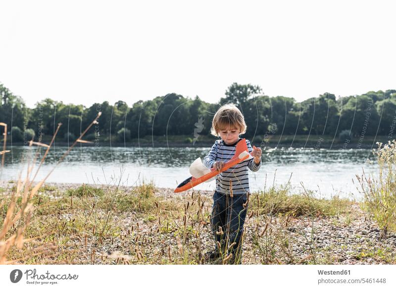 Junge spielt mit einem Spielzeugflugzeug am Flussufer Spielzeugflugzeuge Buben Knabe Jungen Knaben männlich Fluesse Fluß Flüsse Flugzeug Flieger Flugzeuge