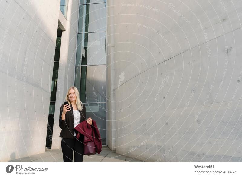 Blonde Geschäftsfrau mit Smartphone im Hintergrund moderne Gebäude geschäftlich Geschäftsleben Geschäftswelt Geschäftsperson Geschäftspersonen Businessfrau