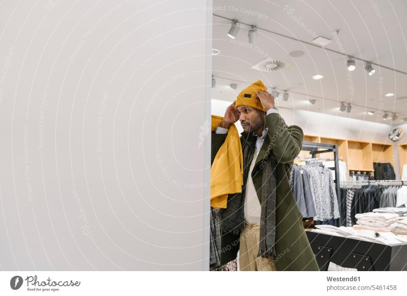 Stilvoller Mann beim Einkaufen in einem Bekleidungsgeschäft, der eine Mütze anprobiert Leute Menschen People Person Personen Kunden Kundschaft geschäftlich