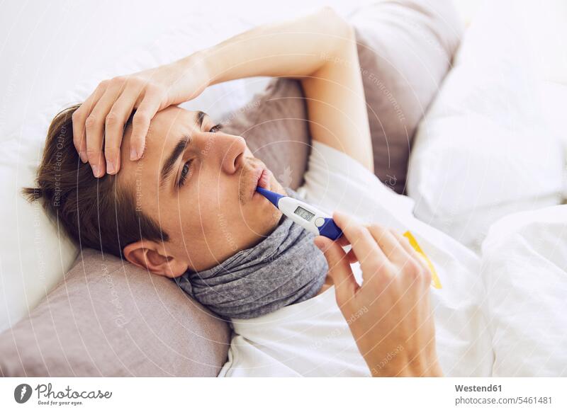 Nahaufnahme eines kranken Mannes mit Thermometer im Mund, der zu Hause auf dem Bett liegt Farbaufnahme Farbe Farbfoto Farbphoto Deutschland Innenaufnahme