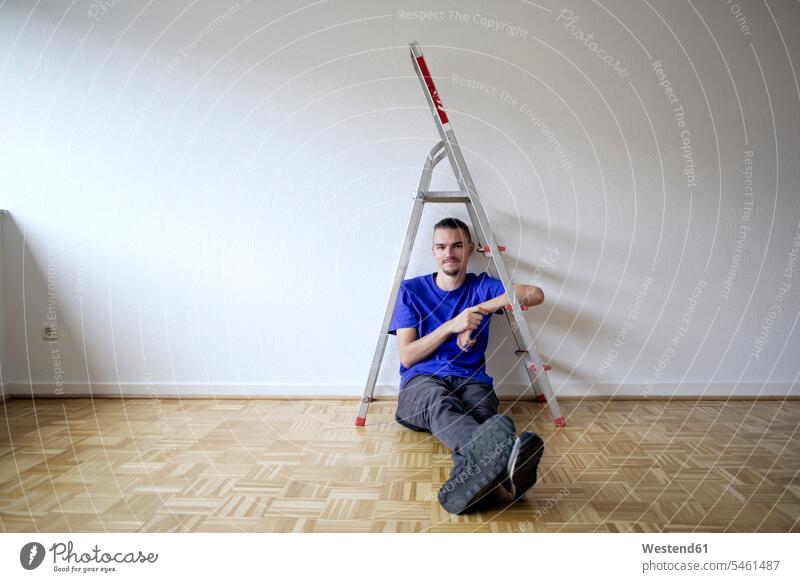 Junger Mann sitzt in einer leeren Wohnung T-Shirts Leitern sitzend umziehen zufrieden daheim zu Hause Immobilie Individuell anfangen Anfänge Beginn beginnen