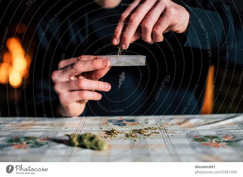 Nahaufnahme der Hände eines Mannes bei der Vorbereitung des Marihuana-Geländes Tabak Zigaretten Papiere daheim zu Hause Realitätsflucht Weltflucht Muße drinnen