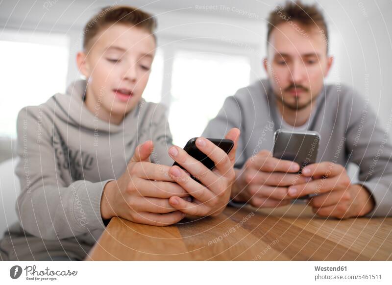 Junger Mann und Teenager benutzen Smartphones im Wohnzimmer Telekommunikation telefonieren Handies Handys Mobiltelefon Mobiltelefone sitzend sitzt entspannen