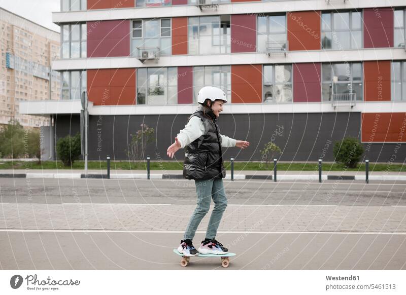 Mädchen in warmer Kleidung beim Skateboarden auf Straße gegen Gebäude Farbaufnahme Farbe Farbfoto Farbphoto Freizeitbeschäftigung Muße Zeit Zeit haben