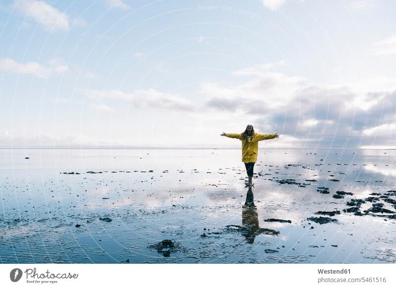 Frau mit ausgestreckten Armen, die sich im Meer am Strand des Naturreservats Hvalnes, Island, spiegeln Farbaufnahme Farbe Farbfoto Farbphoto Außenaufnahme außen