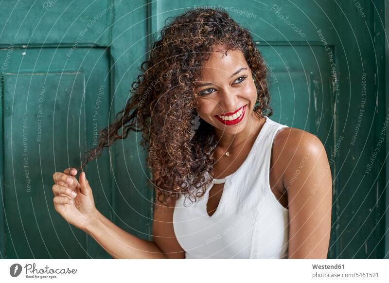Porträt einer lächelnden jungen Frau mit lockigem Haar vor einer grünen Holztür offenes Lächeln lachen offenes Laecheln Kopf zur Seite Kopf geneigt Kopf neigen