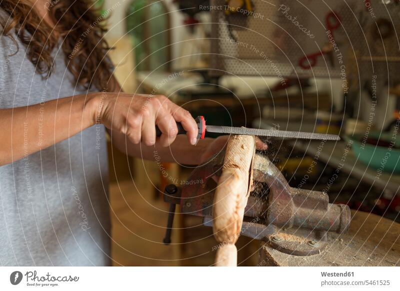 Handwerkerin feilt ein Stück Holz in ihrer Werkstatt feilen Werkstätte Werkstaette Werkstaetten Werkstätten Frau weiblich Frauen Holzstück Holzstuecke Gewerbe