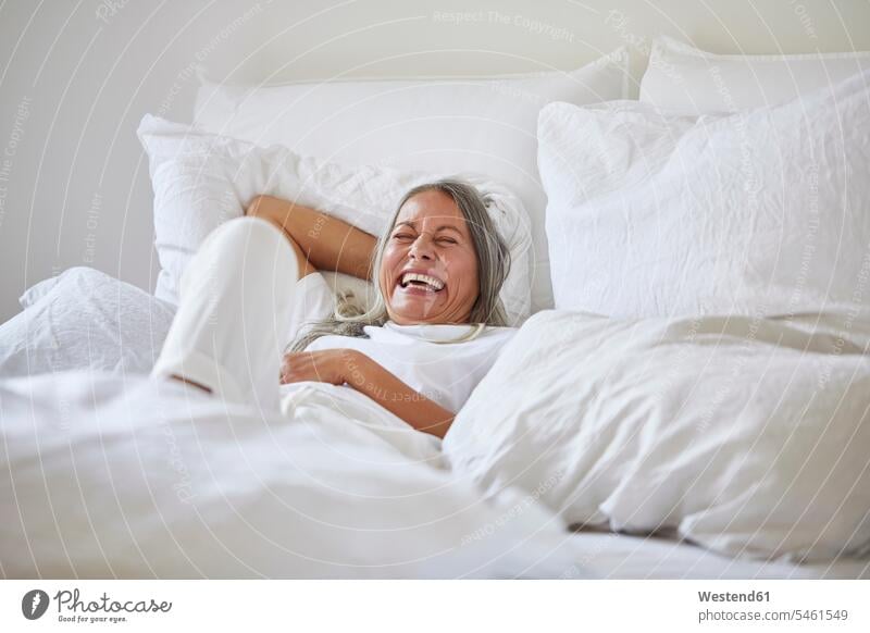 Fröhliche Frau liegt zu Hause auf dem Bett Deutschland Innenaufnahme Innenaufnahmen innen drinnen Tag Tageslichtaufnahme Tageslichtaufnahmen Tagesaufnahme