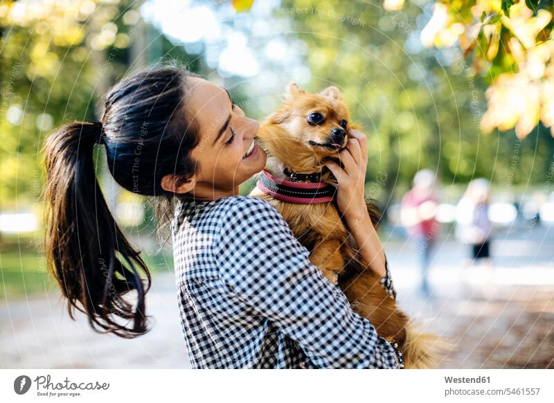 Glückliche junge Frau hält Hund in einem Park Tiere Tierwelt Haustiere Hunde entspannen relaxen Arm umlegen Umarmung Umarmungen freuen Frohsinn Fröhlichkeit