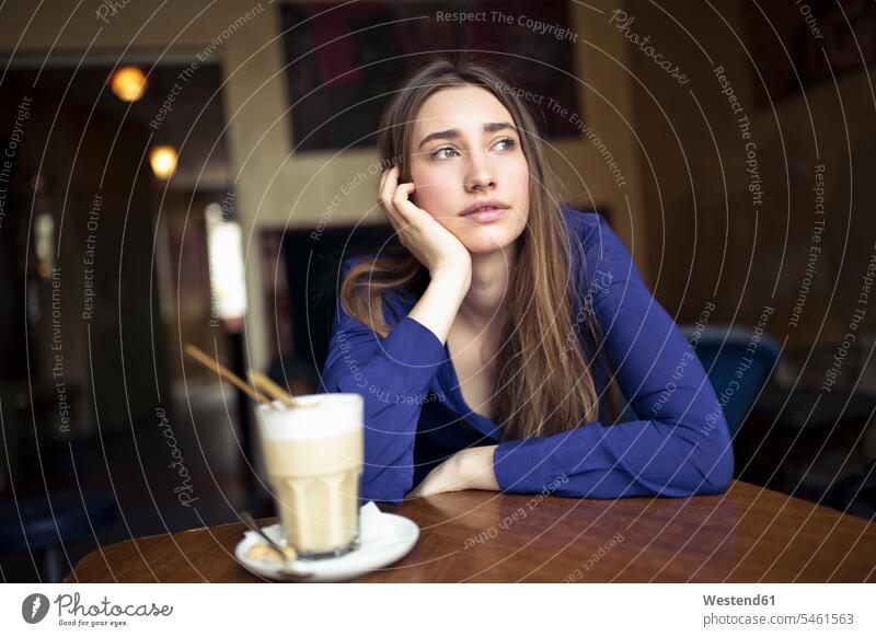 Junge Frau sitzt am Tisch in einem Café und schaut zur Seite Seitenblick Blick zur Seite Tische sitzen sitzend Cafe Kaffeehaus Bistro Cafes Cafés Kaffeehäuser