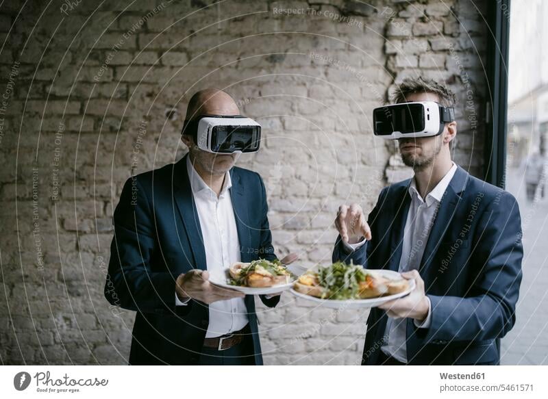 Älterer und mittelgroßer Geschäftsmann mit VR-Brille, der einen Teller mit einer Mahlzeit hält Generation geschäftlich Geschäftsleben Geschäftswelt