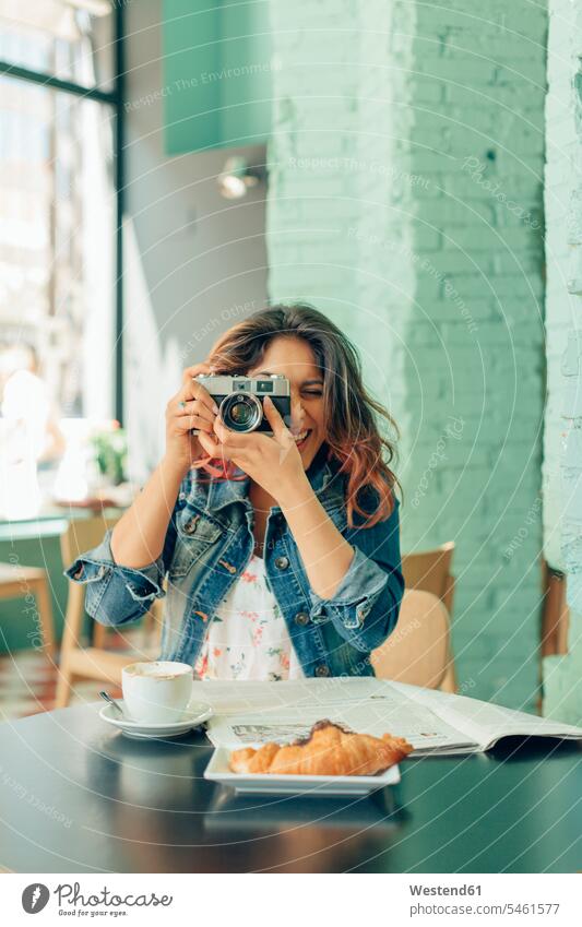 Lachende Frau sitzt im Café und macht Fotos mit der Kamera Cafe Kaffeehaus Bistro Cafes Kaffeehäuser fotografieren Foto machen Fotos machen weiblich Frauen