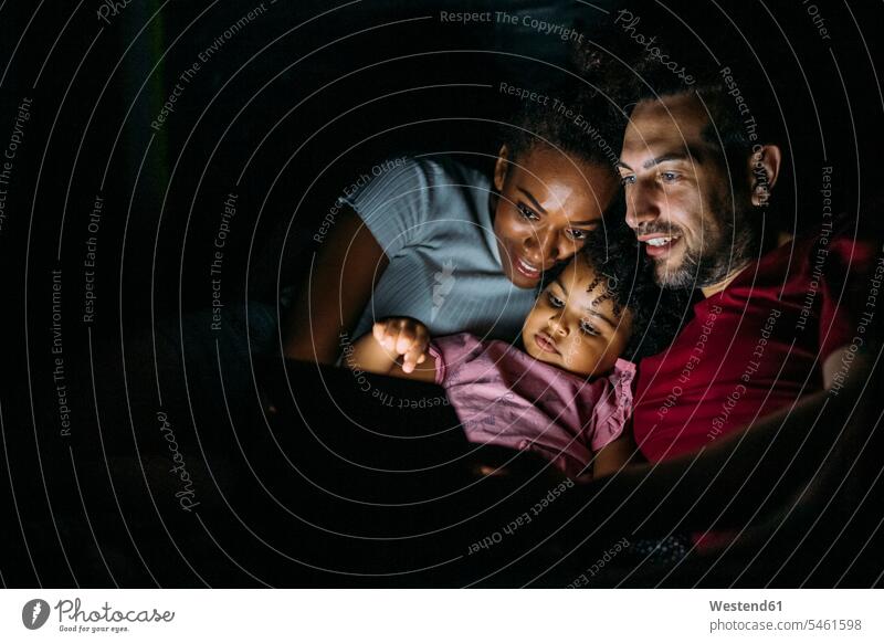 Lächelnde Eltern mit Tochter benutzen digitales Tablet, während sie sich zu Hause im Bett entspannen Farbaufnahme Farbe Farbfoto Farbphoto Freizeitkleidung