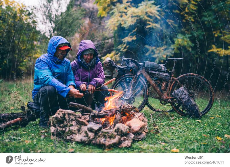 Lachendes Paar mit mit bmx Fahrräder sitzen am Lagerfeuer grillen Würstchen Pärchen Paare Partnerschaft lachen sitzend sitzt Feuer Mensch Menschen Leute People