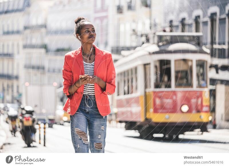 Junge Frau mit Kopfhörern und Smartphone, die sich in der Stadt umsieht, Lissabon, Portugal geschäftlich Geschäftsleben Geschäftswelt Geschäftsperson