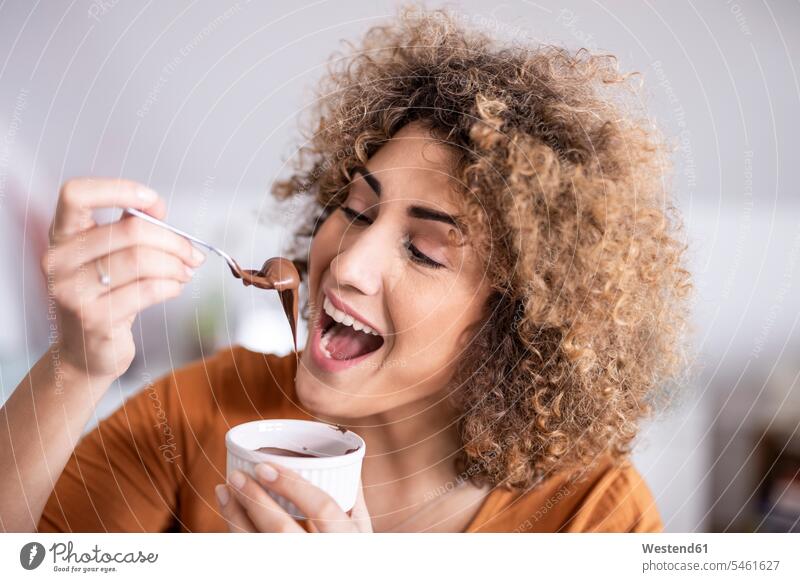 Porträt einer glücklichen Frau, die zu Hause Schokoladencreme isst Leute Menschen People Person Personen gelockt gelockte Haare gelocktes Haar lockig
