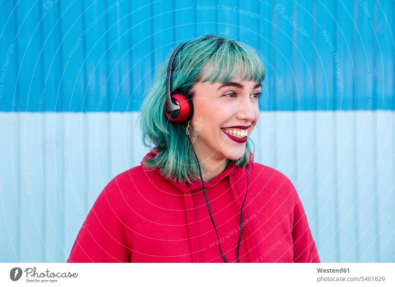 Porträt einer lachenden jungen Frau mit blau gefärbtem Haar, die mit Kopfhörern Musik hört Kopfhoerer Portrait Porträts Portraits weiblich Frauen Haare faerben