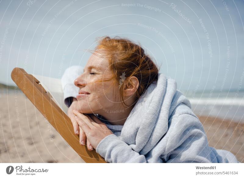 Lächelnde Frau, die im Liegestuhl liegt und ein Sonnenbad am Strand genießt Liegestühle Beach Straende Strände Beaches weiblich Frauen genießen geniessen Genuss