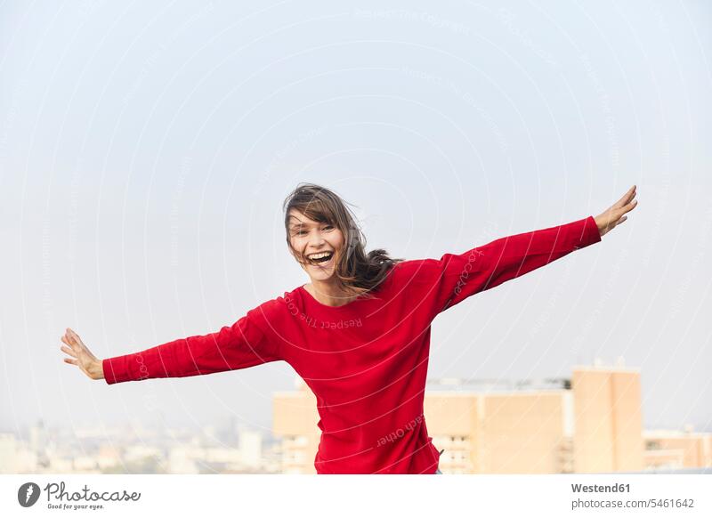 Reife Frau lacht mit ausgestreckten Armen, während sie auf der Gebäudeterrasse gegen den klaren Himmel steht Farbaufnahme Farbe Farbfoto Farbphoto Außenaufnahme