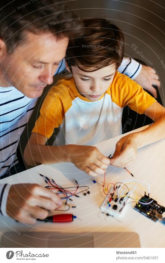 Vater und Sohn beim Zusammenbau eines elektronischen Baukastens elektrisch Bausatz zusammenbauen Kind Familie Mensch Eltern Tisch klug Kabel Einfallsreichtum