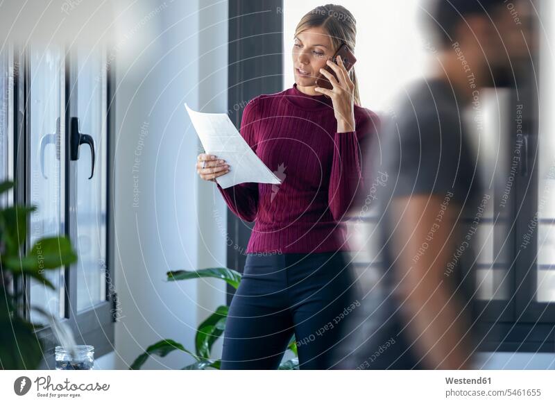 Geschäftsfrau spricht über Smartphone, während ein männlicher Kollege ins Büro geht Farbaufnahme Farbe Farbfoto Farbphoto Spanien Innenaufnahme Innenaufnahmen