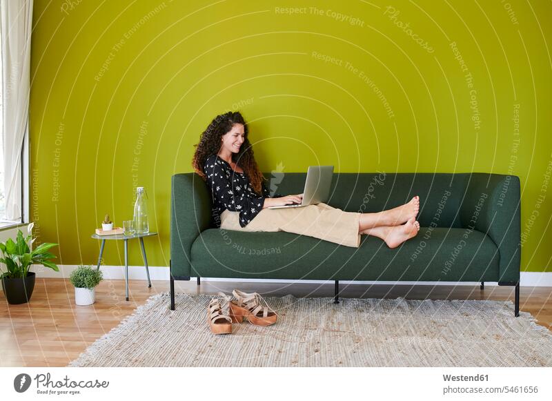 Lächelnde junge Geschäftsfrau mit Laptop auf der Couch im modernen Büro Job Berufe Berufstätigkeit Beschäftigung Jobs geschäftlich Geschäftsleben Geschäftswelt