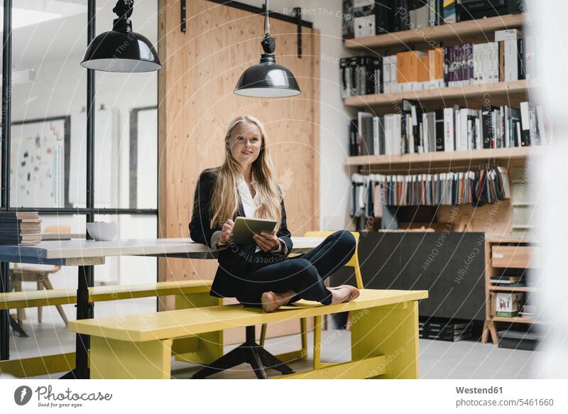 Junge Geschäftsfrau sitzt auf einer Bank in einem Loft-Büro und benutzt ein Tablett Job Berufe Berufstätigkeit Beschäftigung Jobs geschäftlich Geschäftsleben