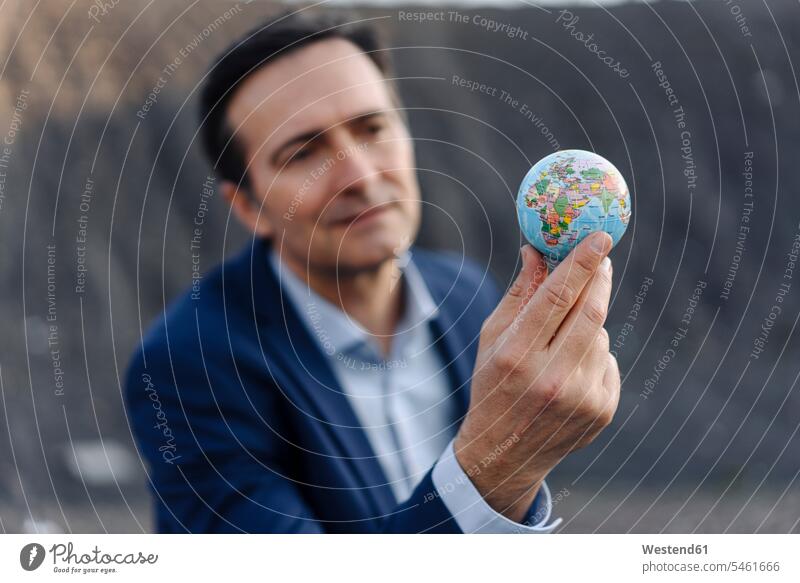 Ein reifer Geschäftsmann hält einen Globus auf einer stillgelegten Minendeponie Leute Menschen People Person Personen Europäisch Kaukasier kaukasisch 1