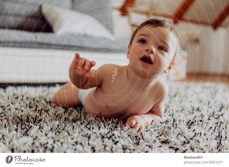 Glückliches Baby spielt auf Teppich liegen liegend liegt Babies Babys Säuglinge Kind Kinder krabbeln kriechen Mensch Menschen Leute People Personen braune Haare