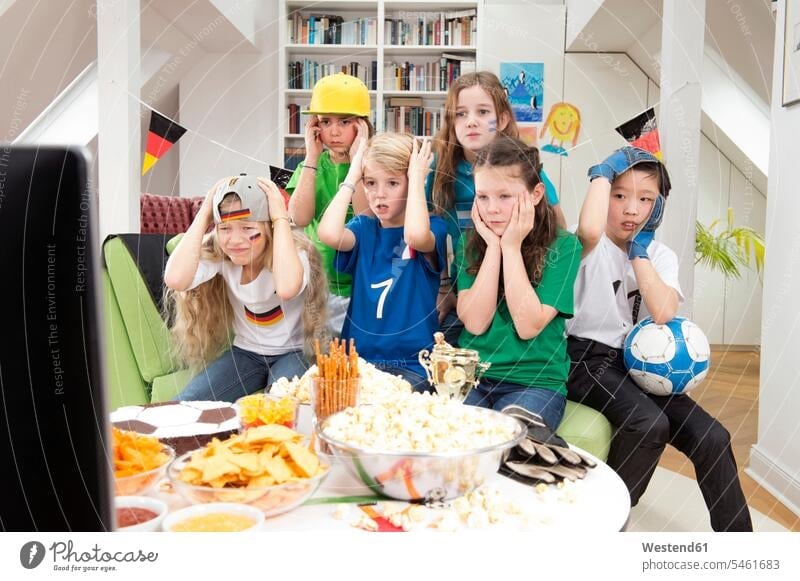 Gruppe von Kindern schaut sich die Fussball-Weltmeisterschaft mit einem Tisch voller Süssigkeiten und Snacks an Fahne Fahnen Zuhause zu Hause daheim spannend
