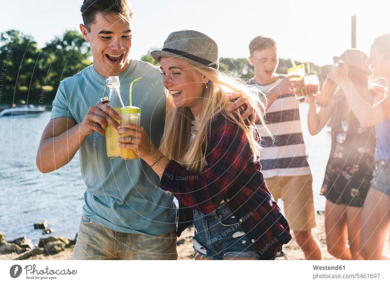 Gruppe glücklicher Freunde beim Spaziergang am Flussufer beim Anstossen mit Getränken Glück glücklich sein glücklichsein Getraenk Getraenke Gruppe von Menschen
