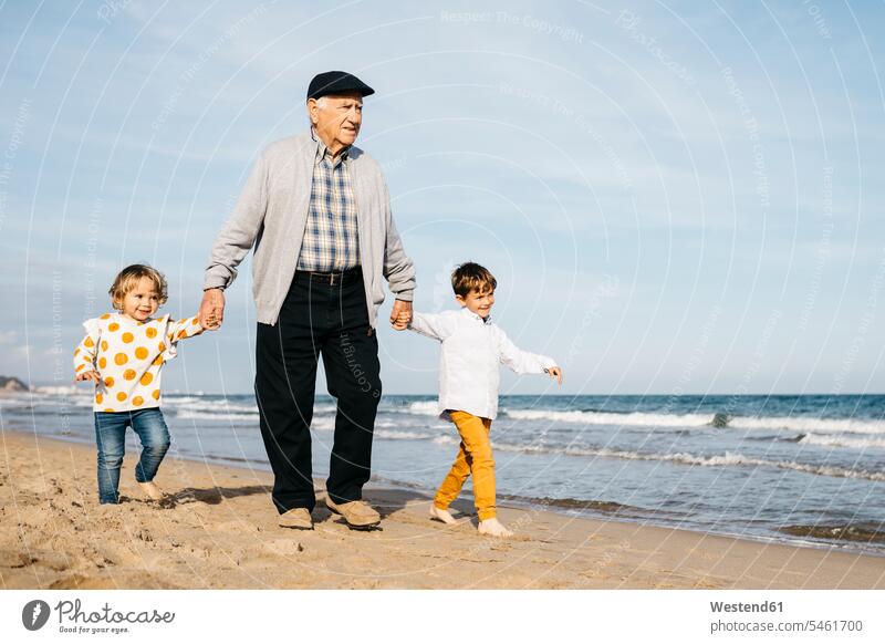 Großvater spaziert mit seinen Enkelkindern Hand in Hand am Strand Urgroßvater Uropa Uropas Urgroßväter Bruder Brüder Enkelsöhne Enkelsohn Enkelin Enkeltochter