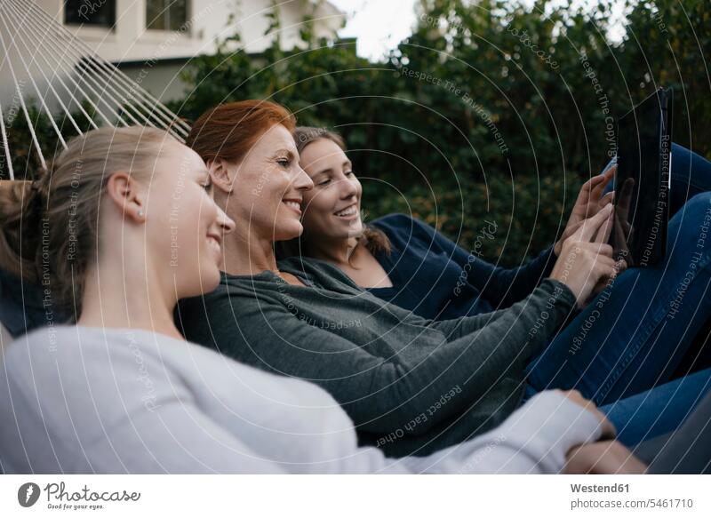 Glückliche Mutter mit zwei Teenager-Mädchen liegen in der Hängematte im Garten im Herbst mit Tablet Tablet Computer Tablet-PC Tablet PC iPad Tablet-Computer