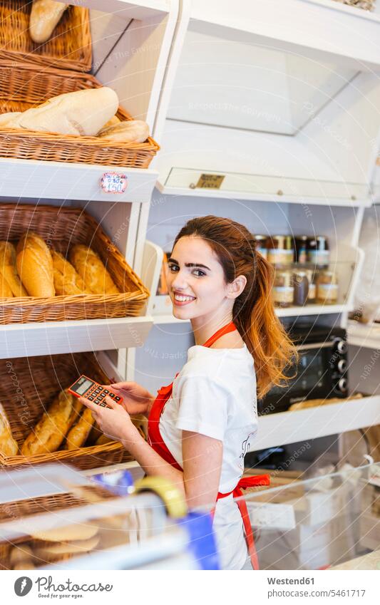 Junge Frau, die in einer Bäckerei arbeitet und einen Taschenrechner benutzt Leute Menschen People Person Personen Europäisch Kaukasier kaukasisch 1 Ein