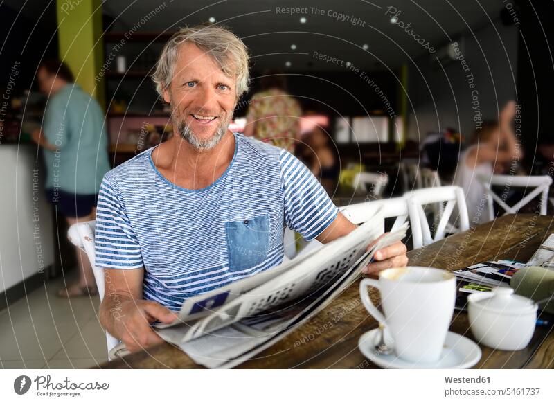 Porträt eines lächelnden reifen Mannes, der in einem Café sitzt und Zeitung liest Portrait Porträts Portraits Zeitungen Cafe Kaffeehaus Bistro Cafes