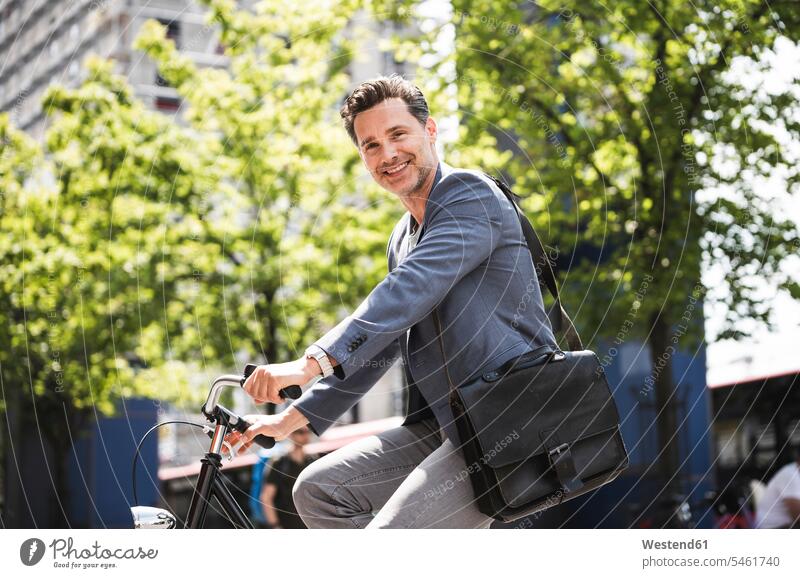 Lächelnder Mann auf dem Fahrrad in der Stadt unterwegs auf Achse in Bewegung fahren staedtisch städtisch Männer männlich radfahren fahrradfahren radeln