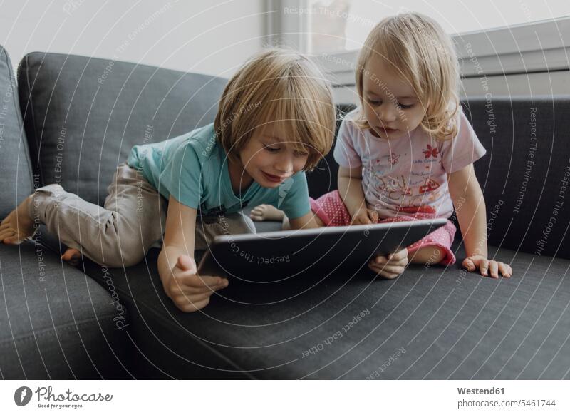 Bruder und kleine Schwester verwenden digitale Tablette auf der Couch zu Hause Zuhause daheim benutzen Tablet Computer Tablet-PC Tablet PC iPad Tablet-Computer