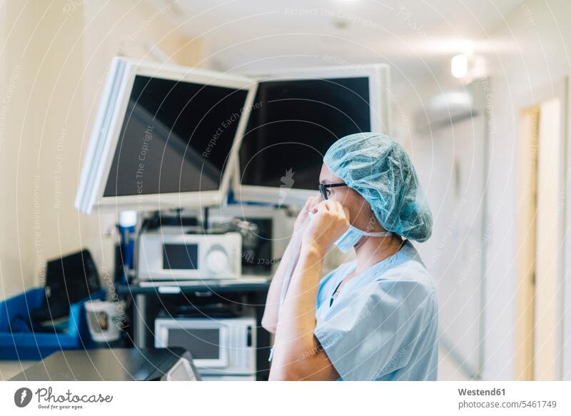 Weiblicher Arzt bindet chirurgische Maske, Vorbereitung für die Operation Europäer Kaukasier Europäisch kaukasisch Brustbild Oberkörper medizinisches Instrument