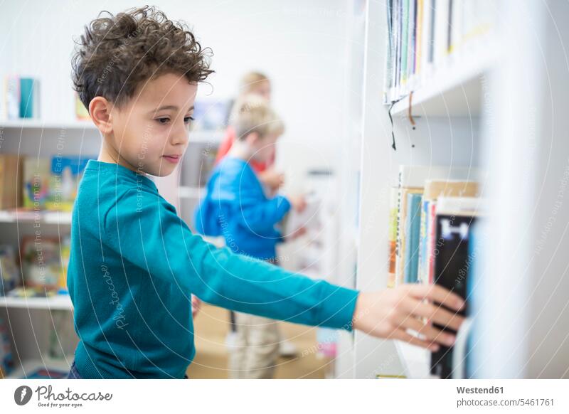 Schuljunge nimmt Buch aus dem Regal in der Schulbibliothek Bücher Ablage Regale nehmen aufnehmen Schule Schulen Schüler Bücherei Wissen Intelligenz klug