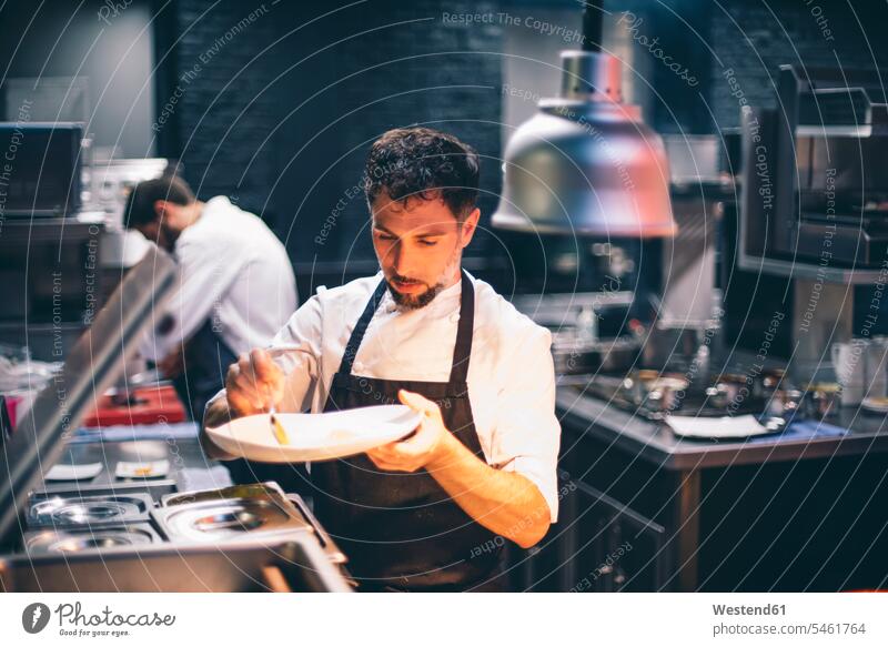 Chefkoch, der in der Küche eines Restaurants Speisen auf einem Teller serviert Job Berufe Berufstätigkeit Beschäftigung Jobs Gastronomie Koeche Kuechenchef