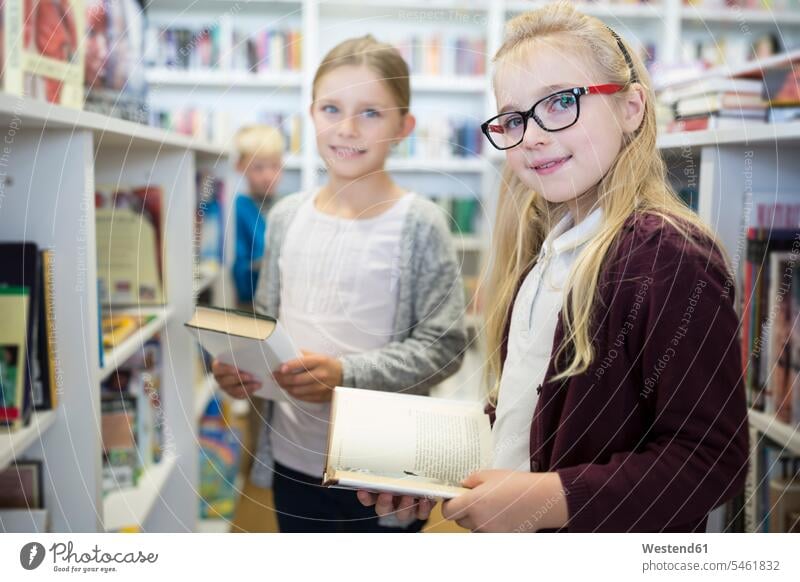 Porträt von zwei lächelnden Schulmädchen mit Büchern in der Schulbibliothek Schülerin Schuelerin Schülerinnen Schuelerinnen Buch Bücherei Schule Schulen