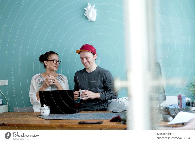 Mutter und Sohn sitzen am Küchentisch, mit Laptop Deutschland Basecap Schirmmuetze Mütze Schirmmütze Muetze Kopfbedeckung Websurfen Im Net surfen Surfen