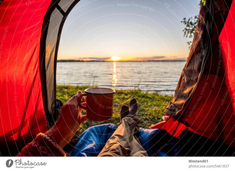 Mann zeltet in Estland und beobachtet den Sonnenuntergang im Zelt liegend See Seen Camping Campen zelten offen auf geöffnet Bein Beine trinken ausruhen Rast
