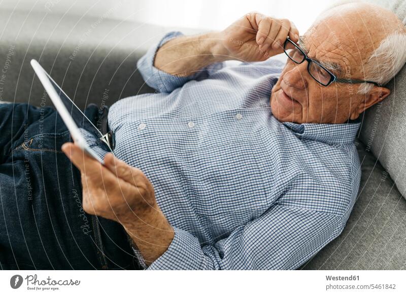 Älterer Mann surft auf einem Tablett im Internet, während er auf dem Sofa liegt Couches Liege Sofas Senior ältere Männer älterer Mann Senioren