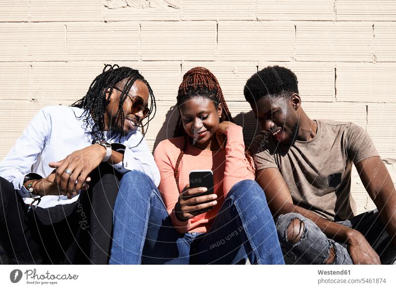 Drei Freunde sitzen zusammen und schauen sich im Freien ein Video auf einem Smartphone an glücklich Glück glücklich sein glücklichsein betrachten betrachtend