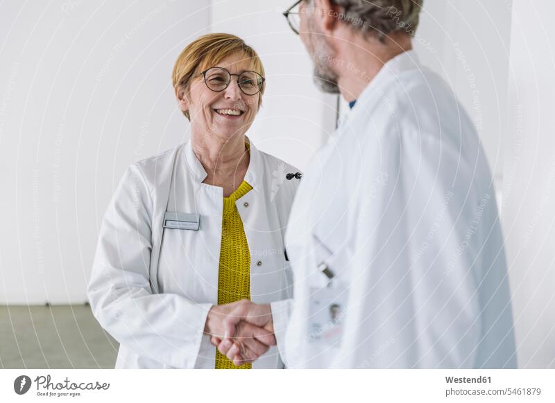 Zwei lächelnde Ärzte beim Händeschütteln Job Berufe Berufstätigkeit Beschäftigung Jobs Brillen begruessen Begrüßung grüßen reden zufrieden stehend steht