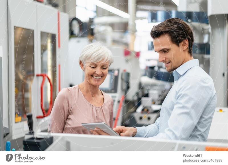 Lächelnder Geschäftsmann und ältere Frau mit Tablet im Gespräch in einer Fabrik sprechen reden lächeln Fabriken weiblich Frauen Businessmann Businessmänner
