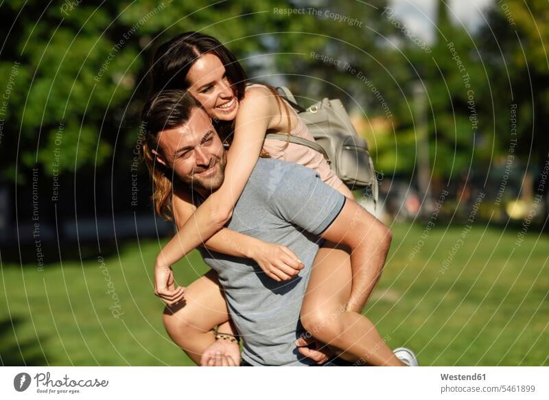 Glücklicher Mann nimmt seine Freundin im Park Huckepack Parkanlagen Parks glücklich glücklich sein glücklichsein tragen transportieren Paar Pärchen Paare